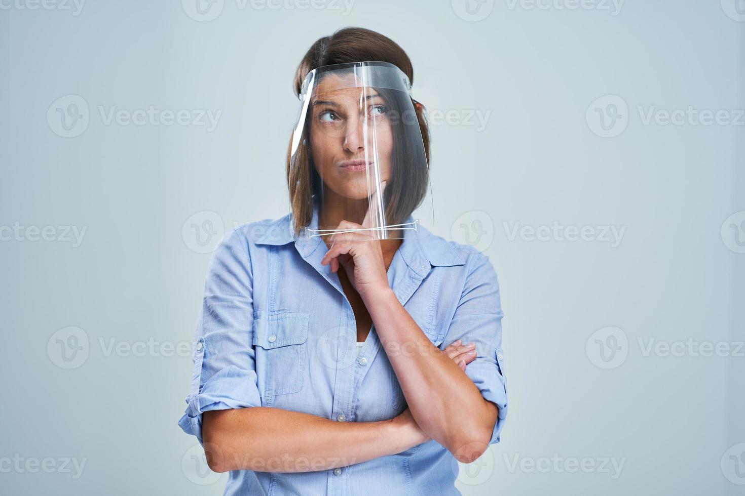 Attractive woman wearing protective shield thinking over white background photo