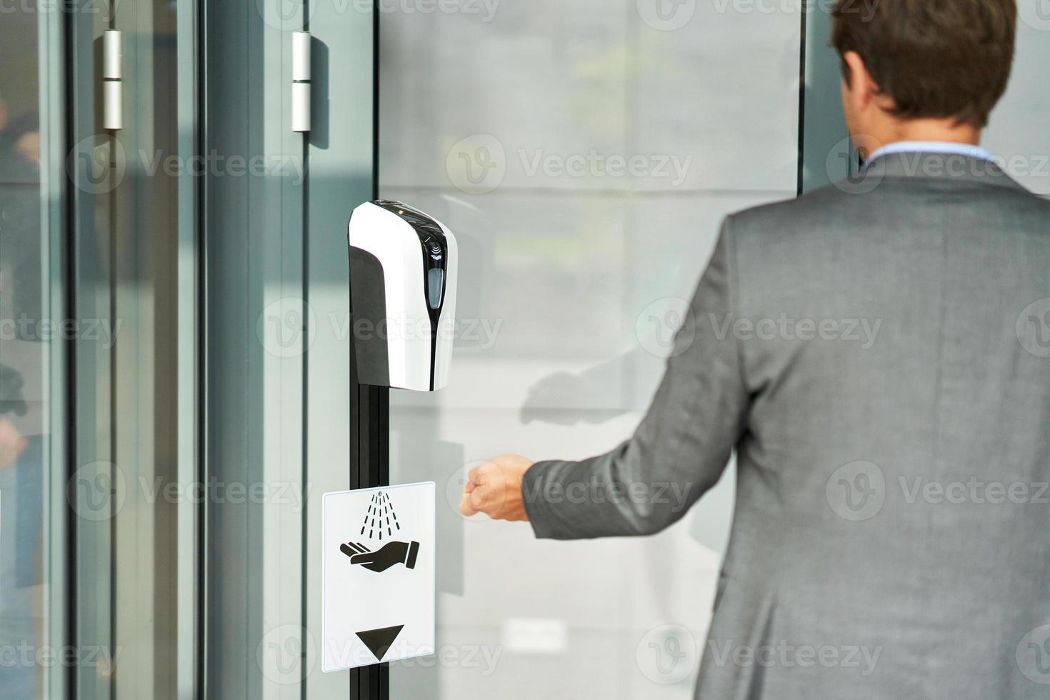 Businessman entering building using hand sanitizer due to covid-19 photo