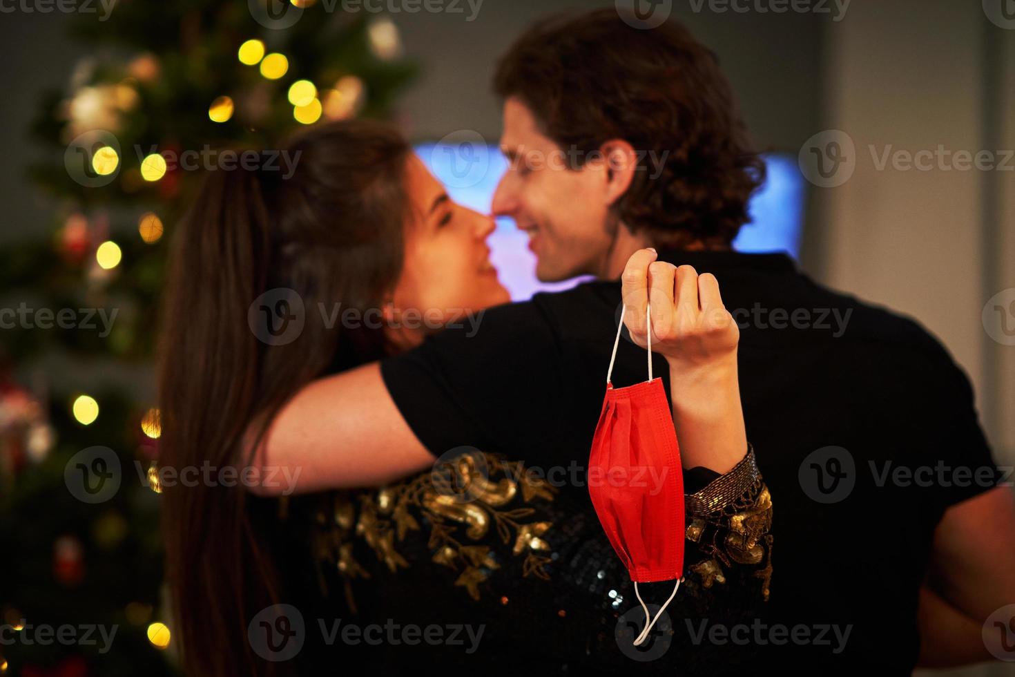 pareja adulta abrazándose sobre el árbol de navidad y sosteniendo una máscara foto