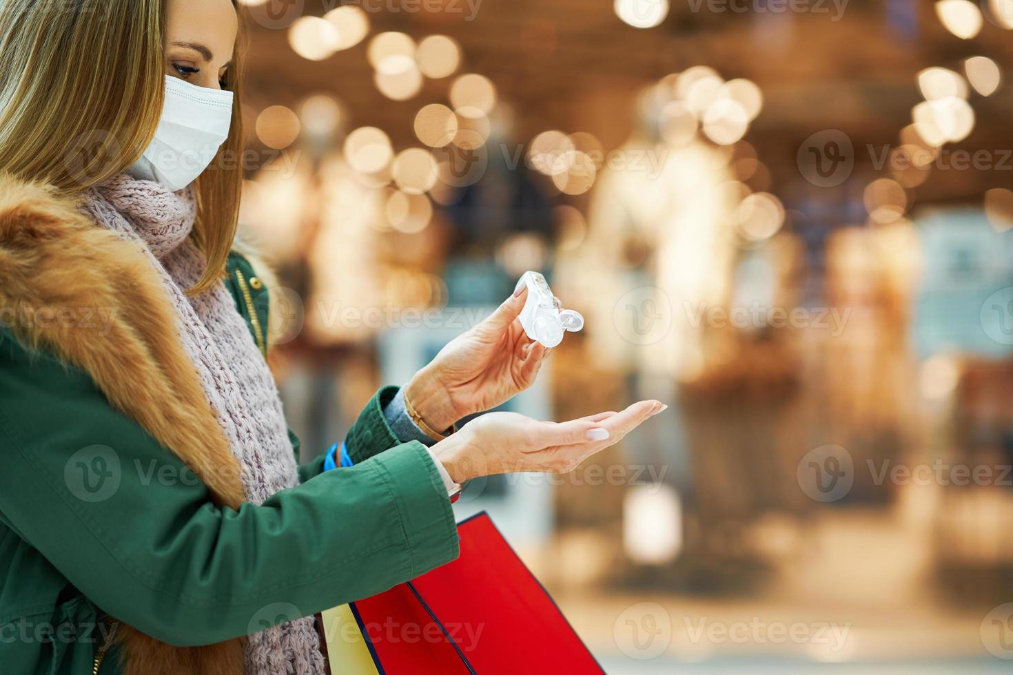 Midsection of adult woman in mall wearing a mask and using hand sanitizer photo
