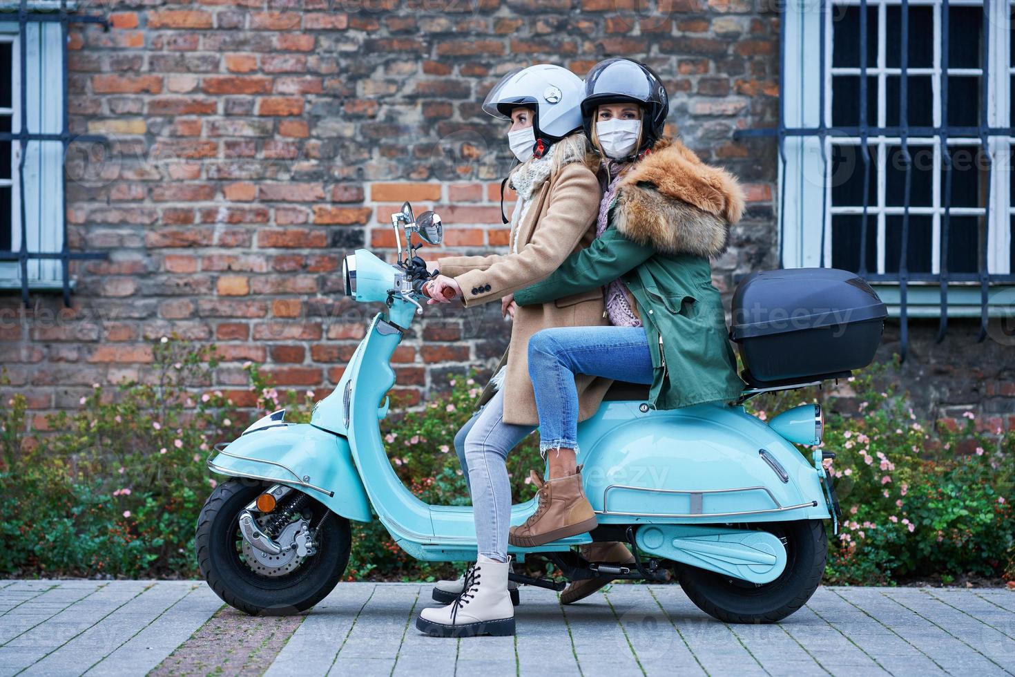 Two women wearing masks and commuting on scooter photo