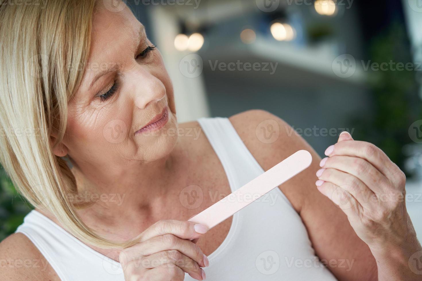 Senior woman using nail file in the bathroom photo