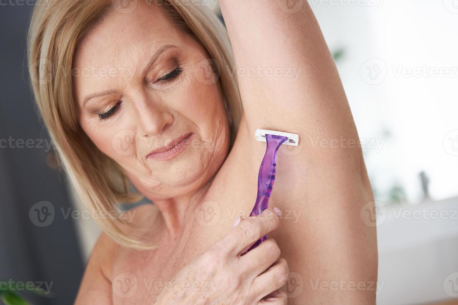 Senior woman shaving armpits in the bathroom photo