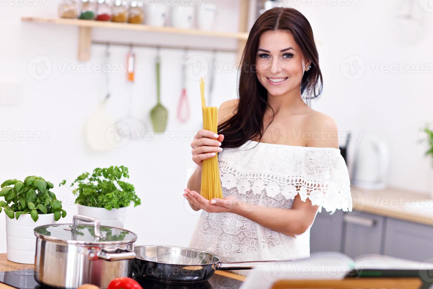 Young woman trying to prepare pasta in kitchen photo