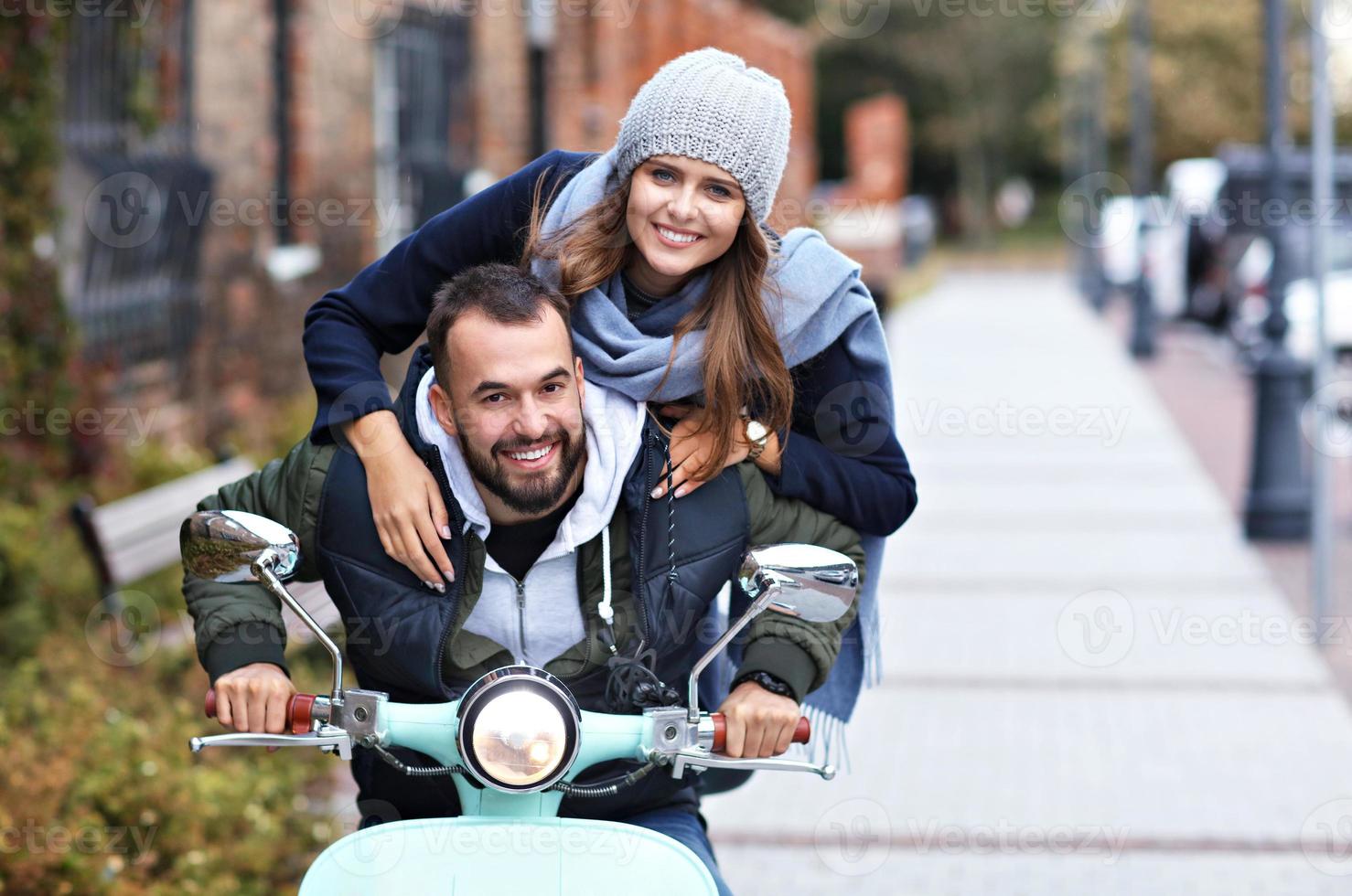 Beautiful young couple smiling while riding scooter in city in autumn photo