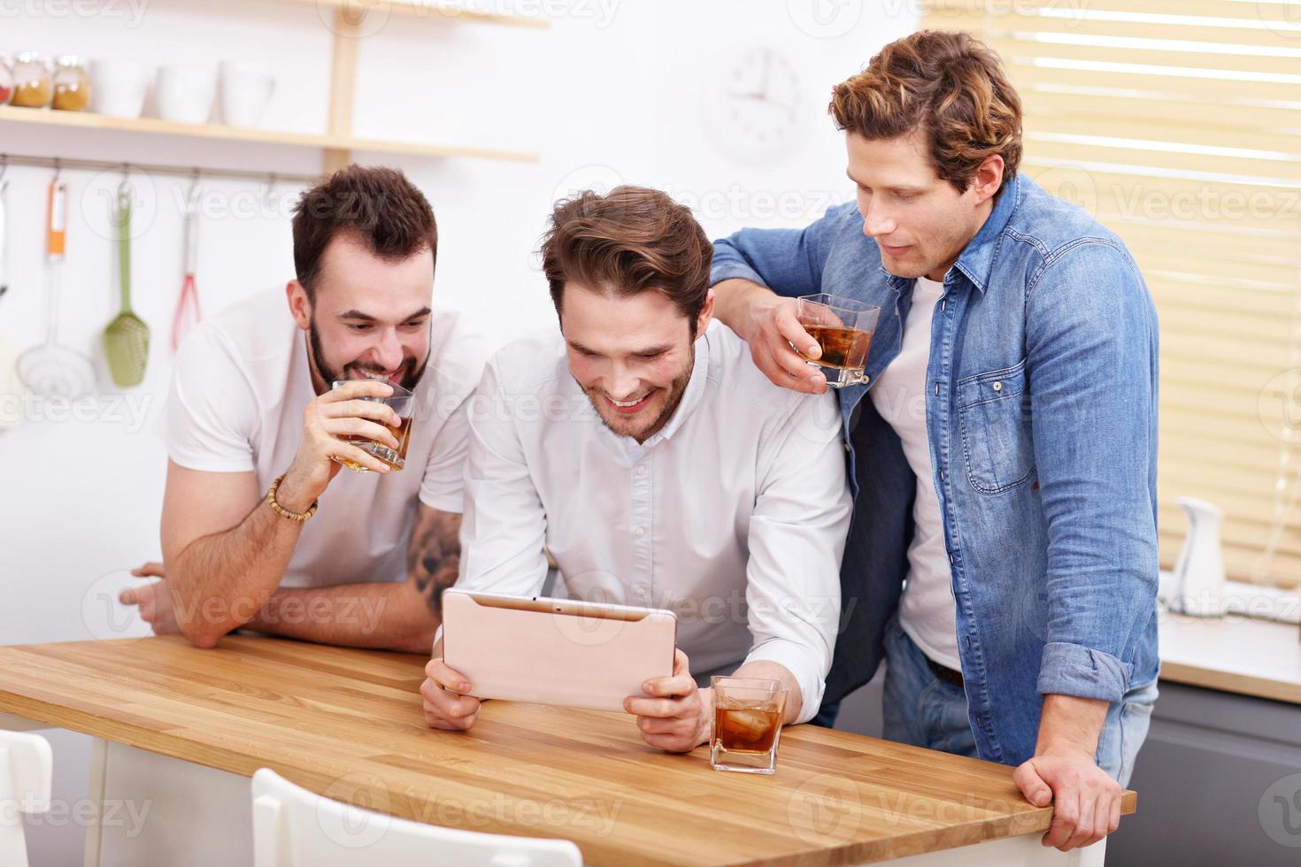 Cheerful friends having fun with smartphone and drinking at home photo