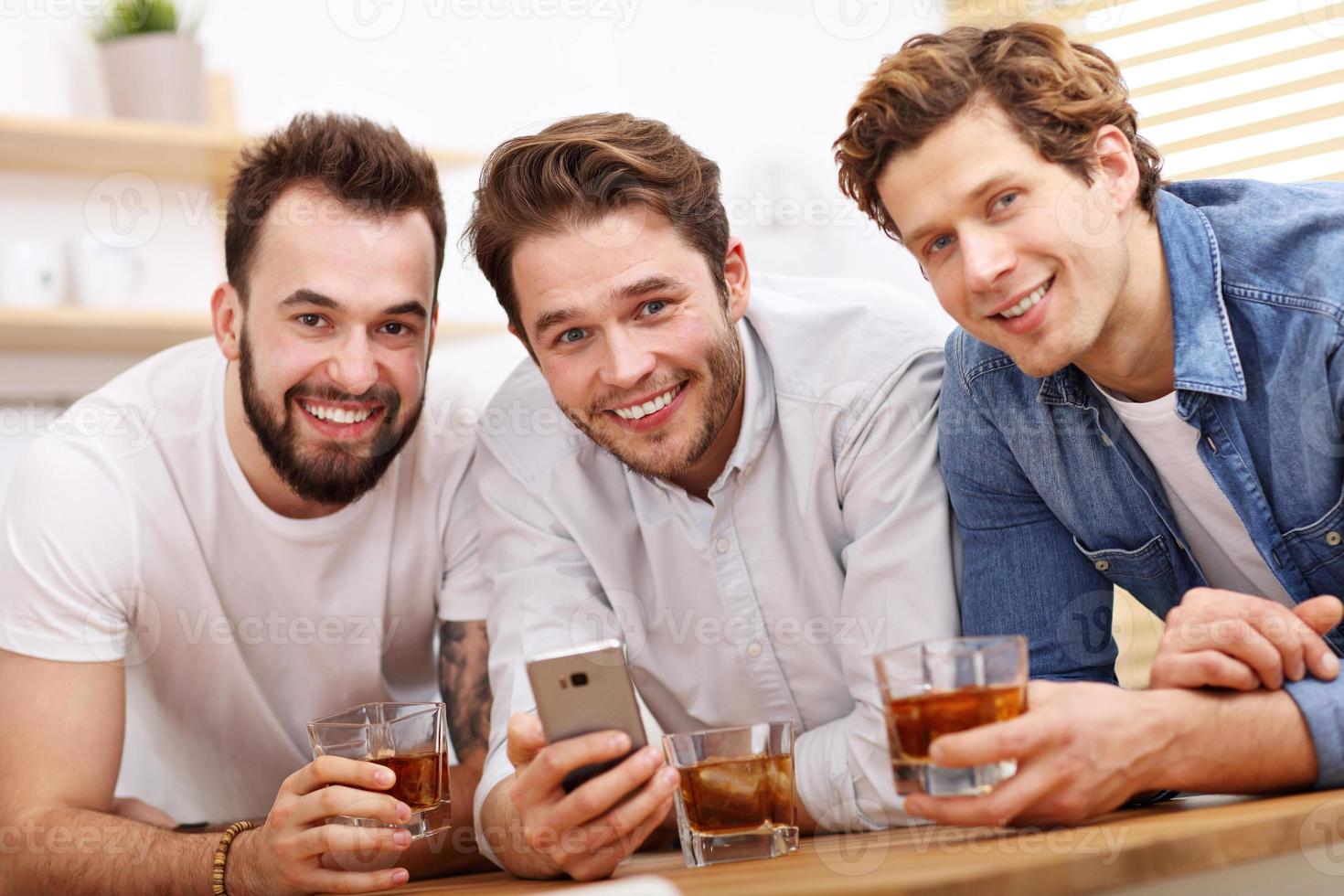 Cheerful friends having fun with smartphone and drinking at home photo