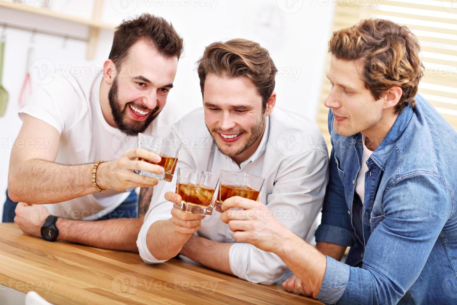 Cheerful friends having fun with smartphone and drinking at home photo