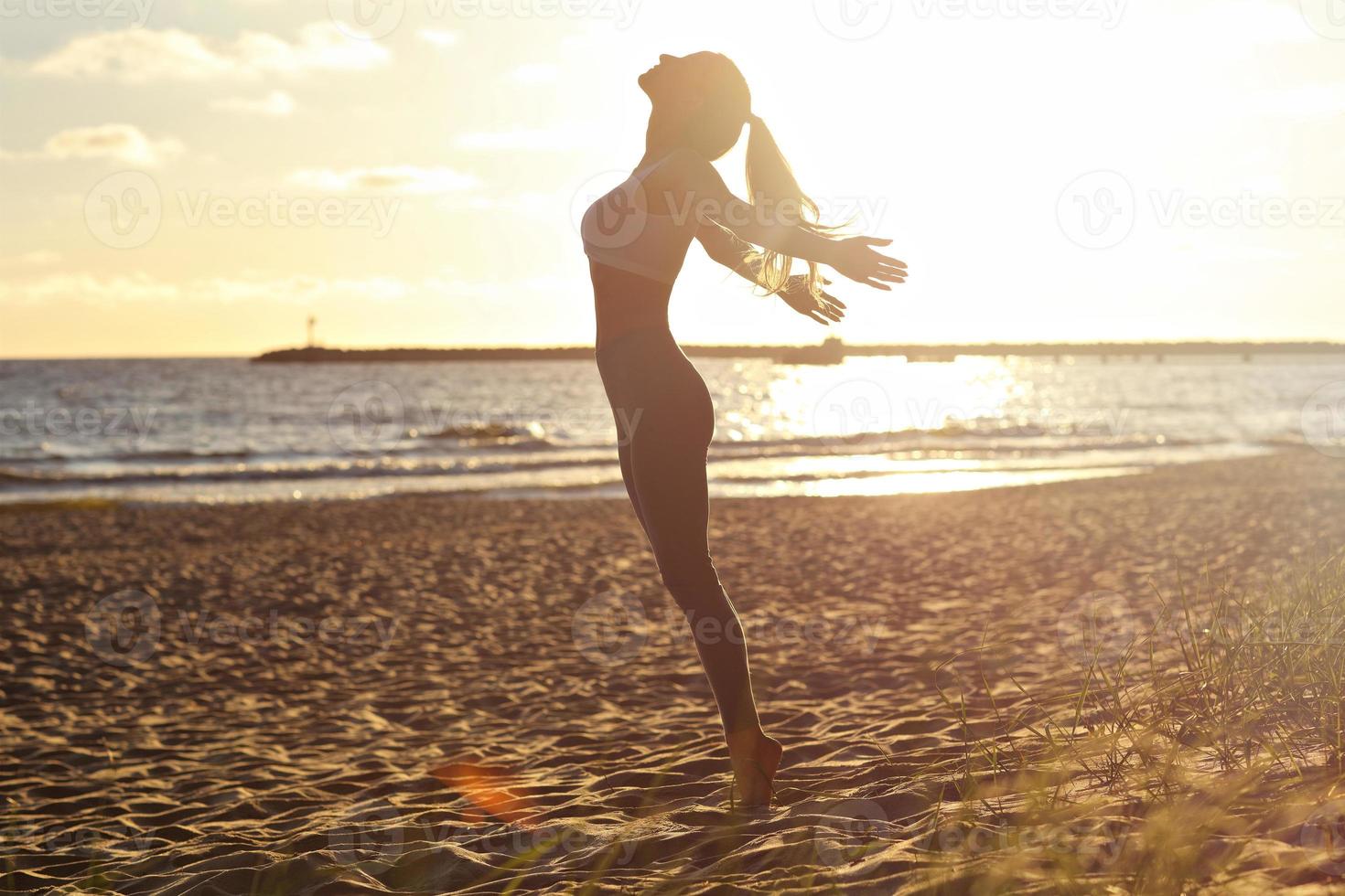 Silhouette young woman practicing yoga on the beach at sunset photo