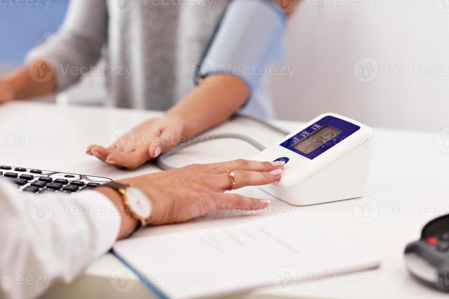 Adult woman having blood pressure test during visit at female doctor's office photo