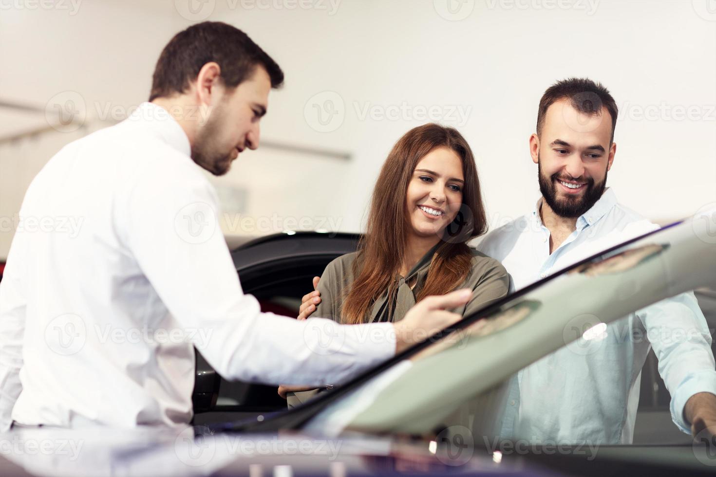 Confident young salesman explaining car features to the young attractive owners photo