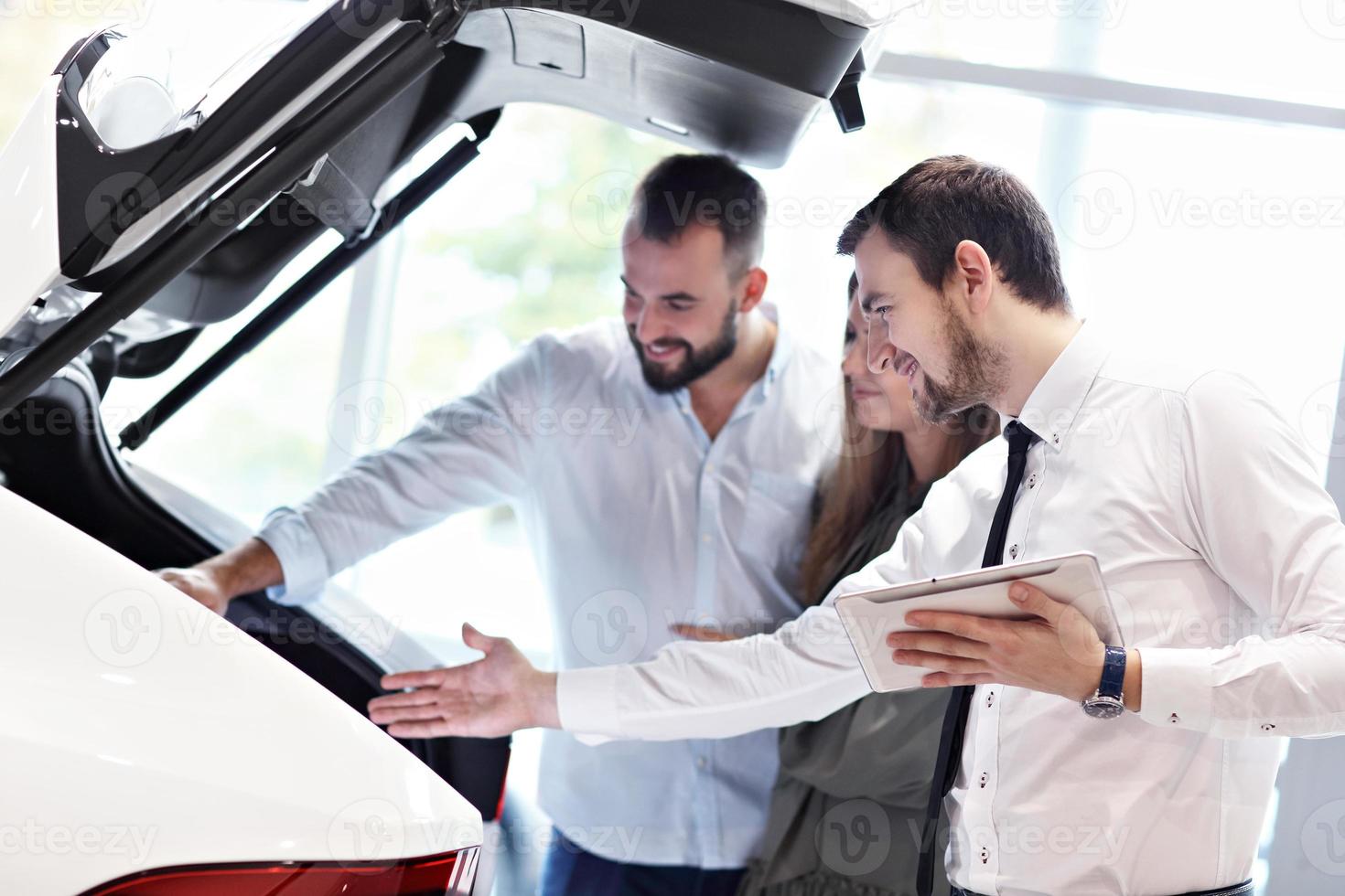 Confident young salesman explaining car features to the young attractive owners photo