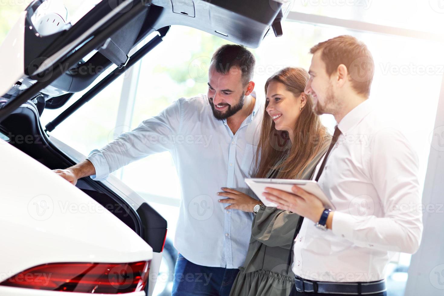 Confident young salesman explaining car features to the young attractive owners photo