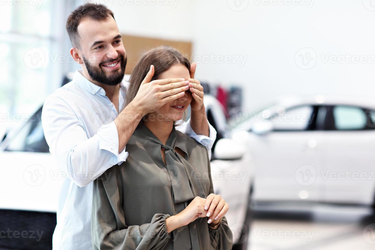 Adult man making surprise to beautiful woman in car showroom photo