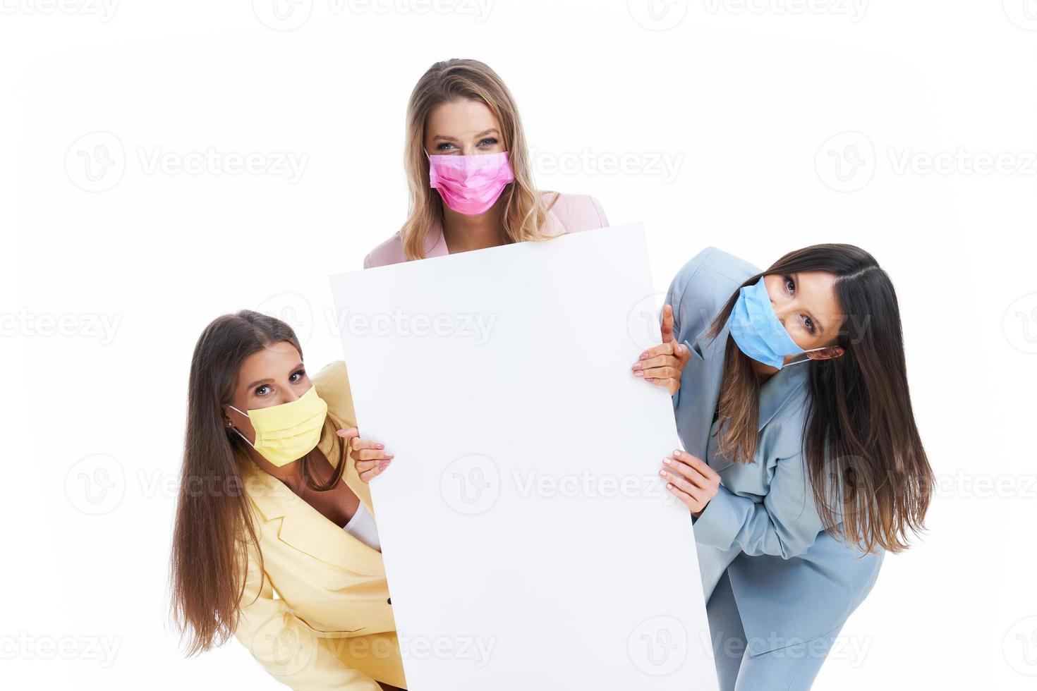 Three women in pastel suits holding billboard posing over white background photo