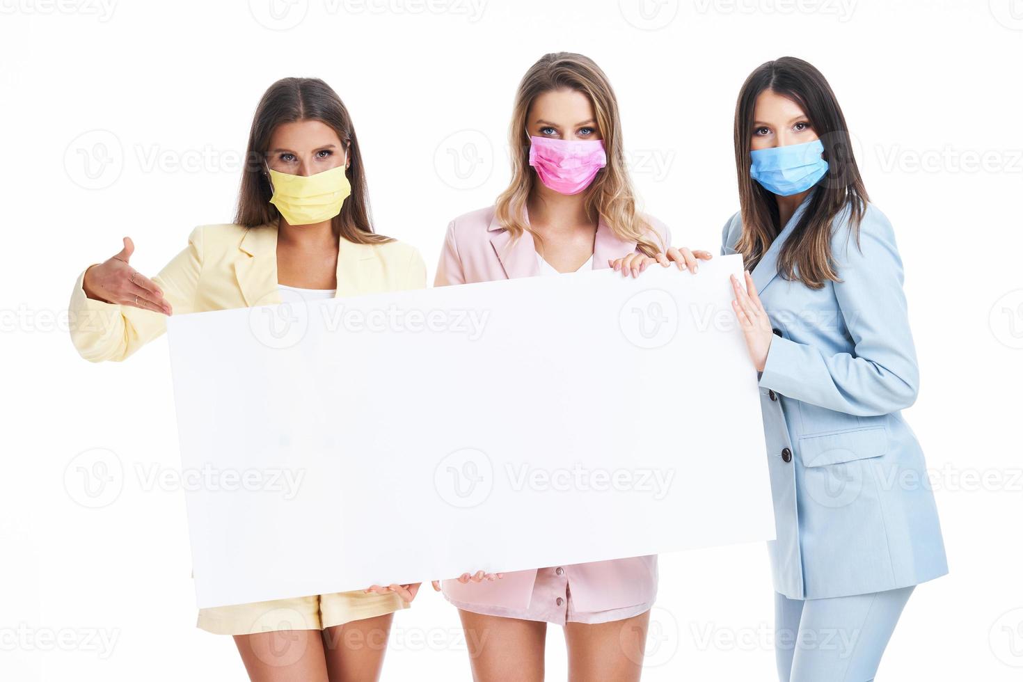 Three women in pastel suits holding billboard posing over white background photo