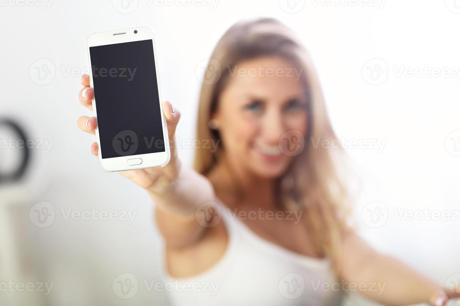 Happy woman with smartphone on sofa photo