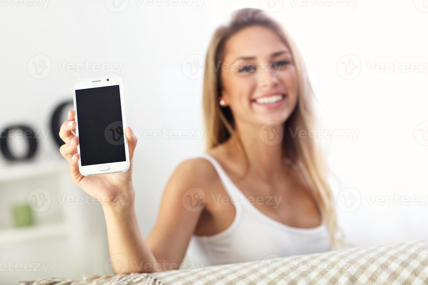 Happy woman with smartphone on sofa photo