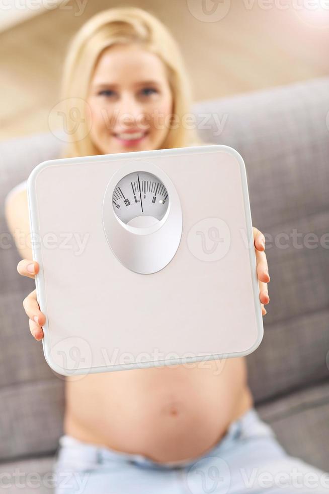 Happy pregnant woman resting on sofa with bathroom scale photo
