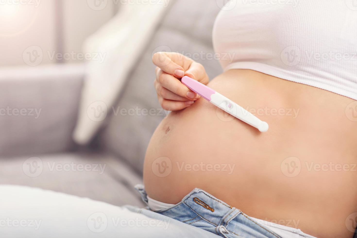 Happy pregnant woman resting on sofa with pregnancy test photo