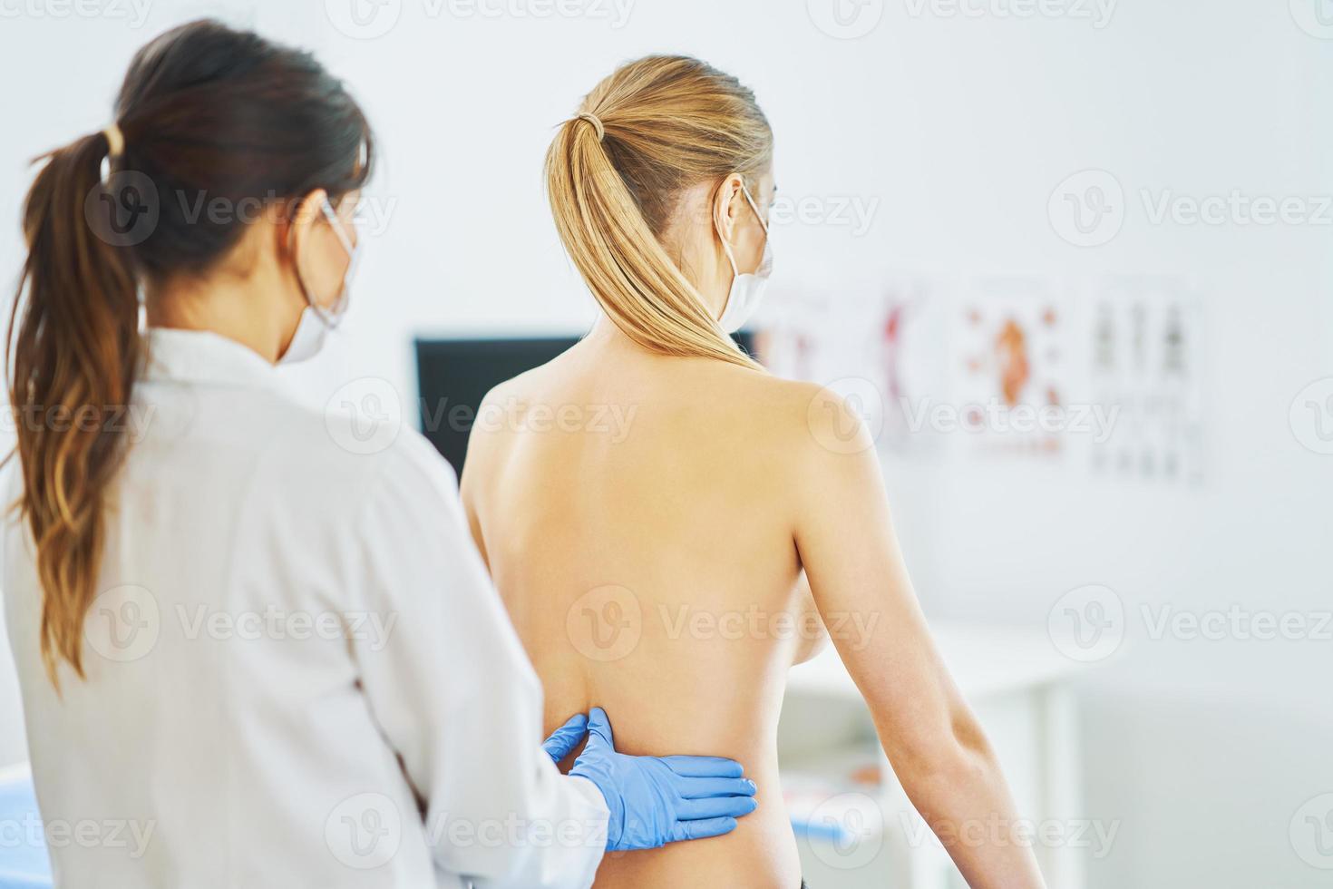 Doctor in mask checking up breast to her patient photo