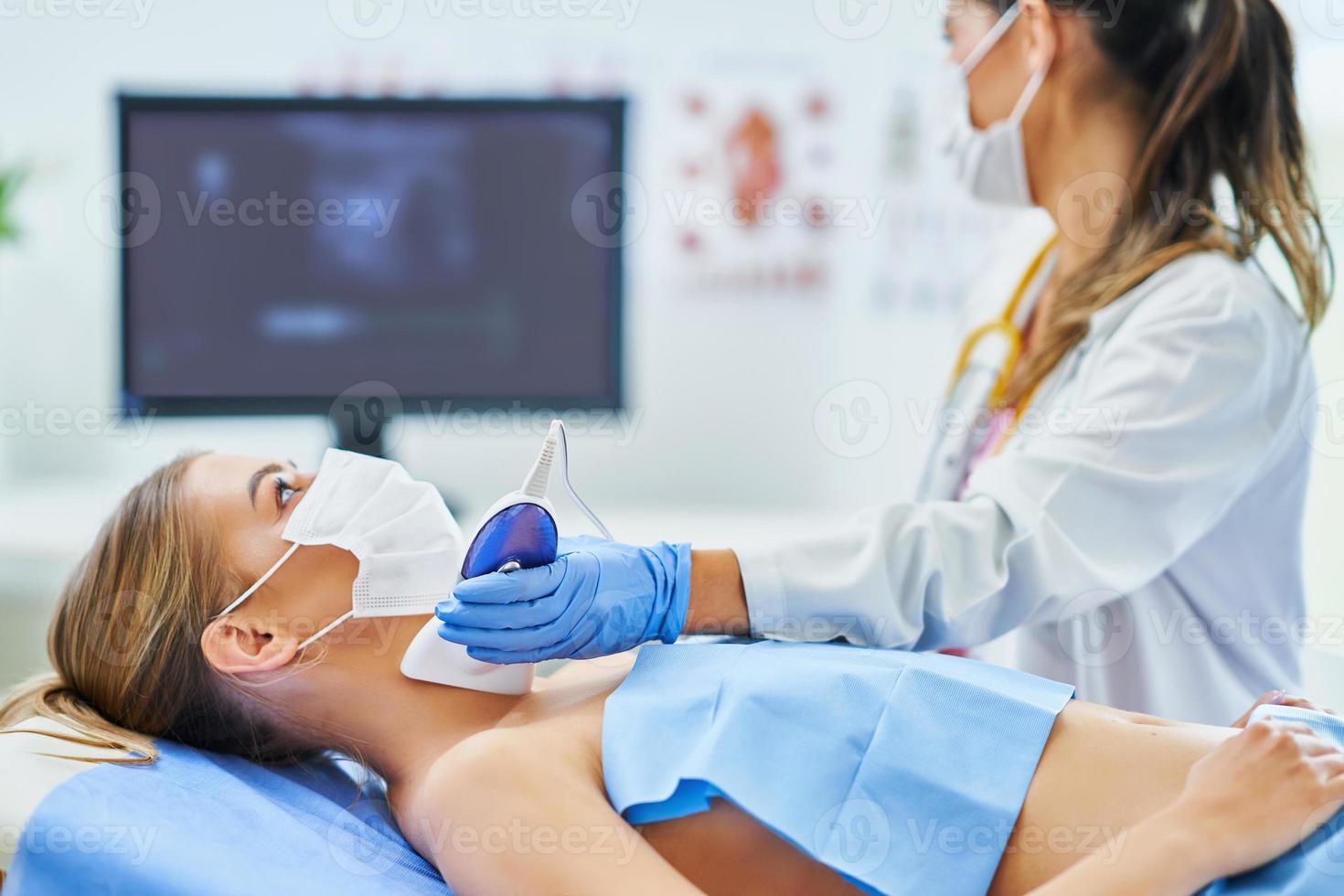 Doctor in mask checking thyroid to her female patient photo
