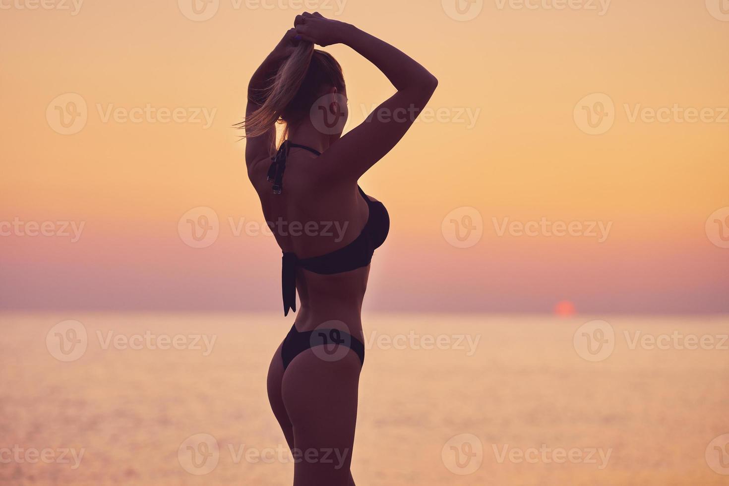 Silhouette of sexy woman posing at sunrise at the beach photo