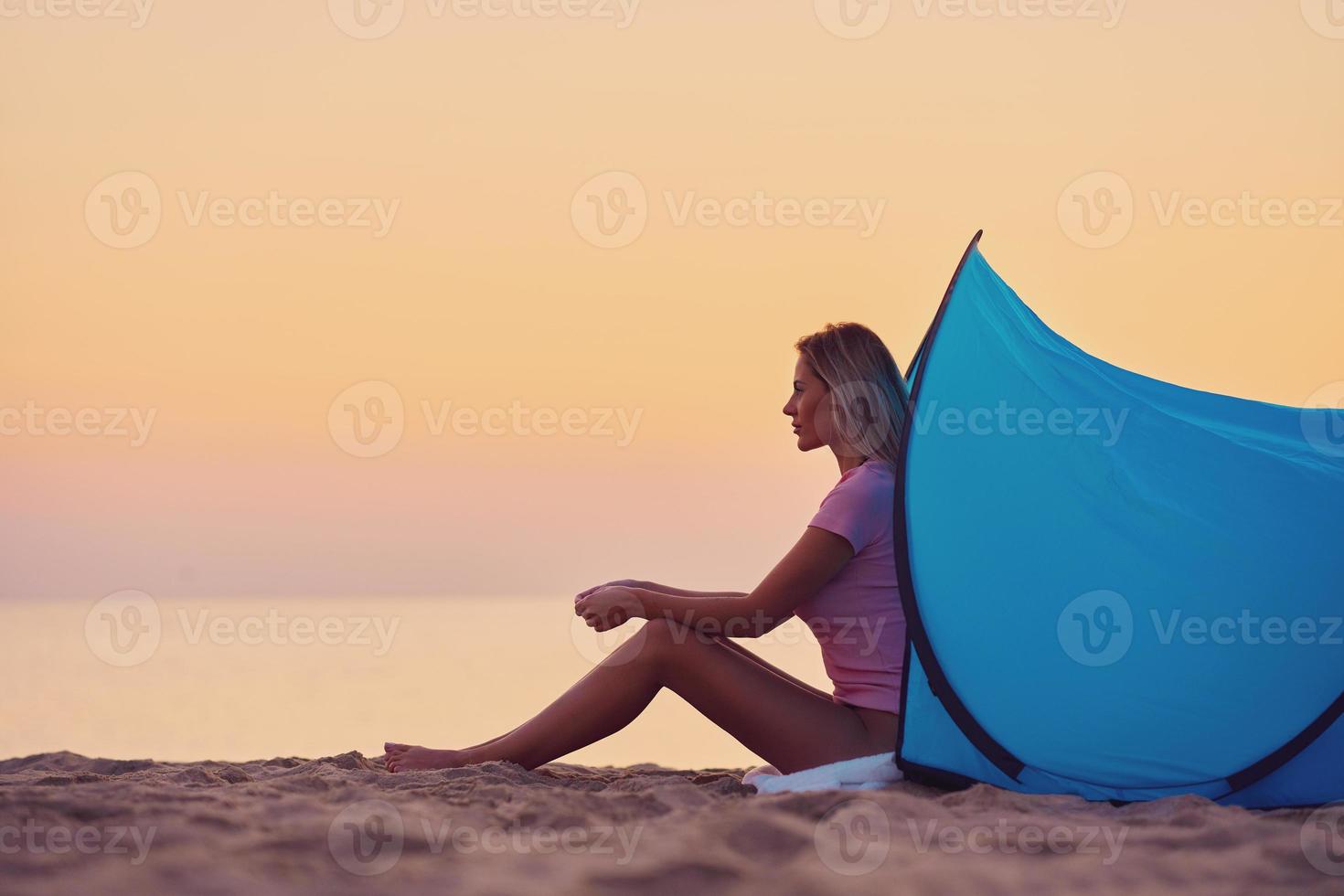 Silhouette of young woman in front of a tent at the beach at sunrise photo