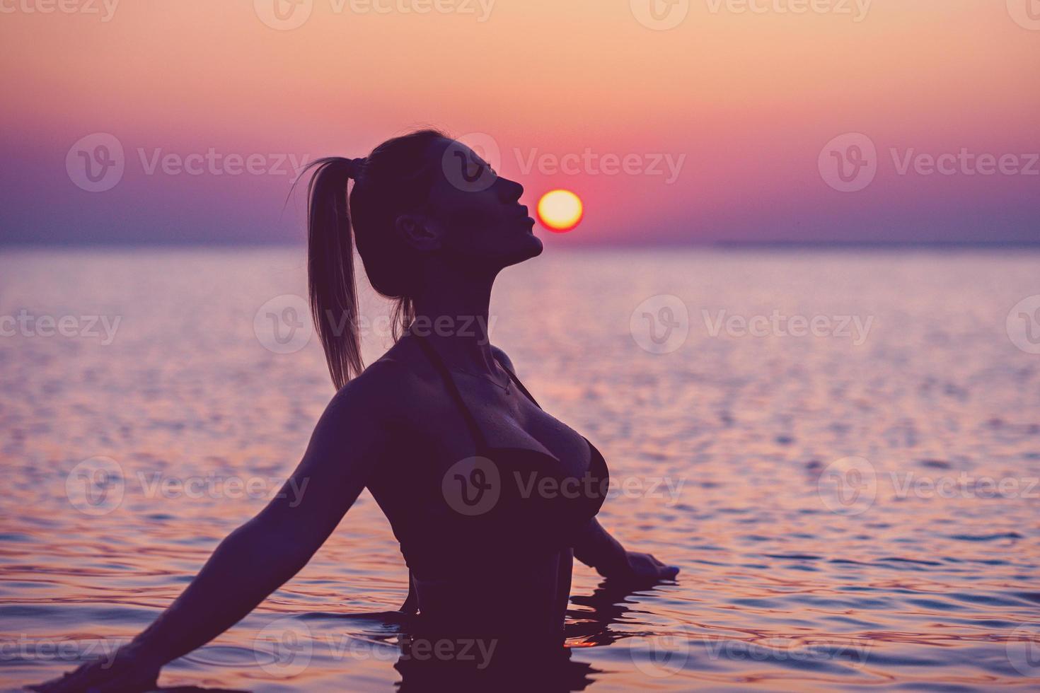 Silhouette of young woman practicing yoga on the beach at sunrise photo