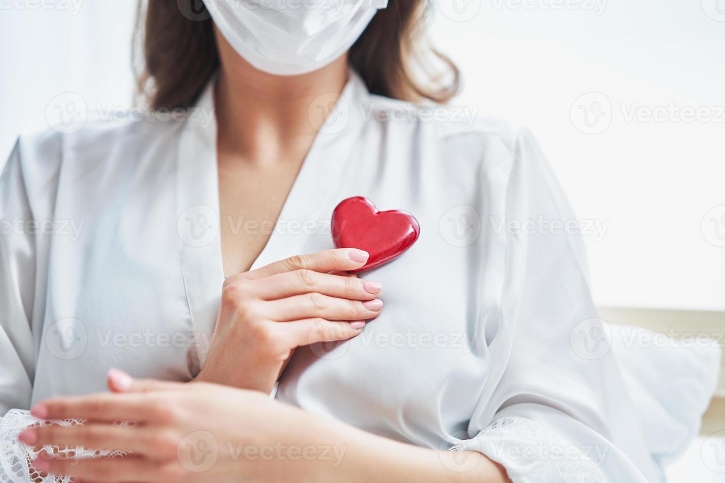 Adult woman in mask showing heart shape at home Covid-19 concept photo