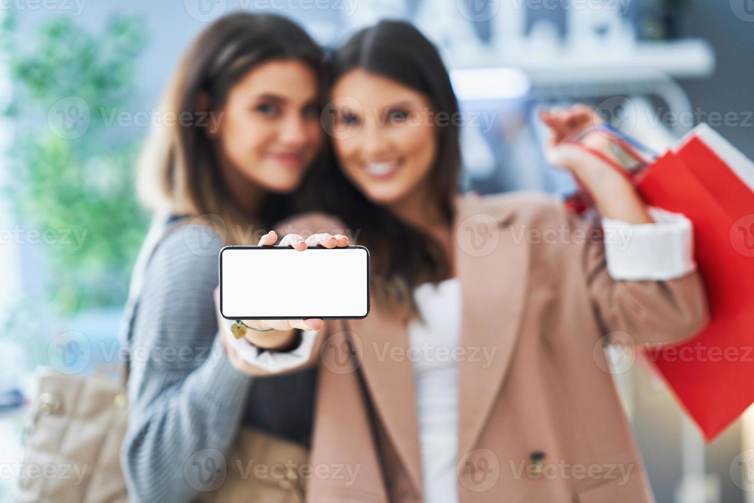 Two happy girls on shopping holding phone photo