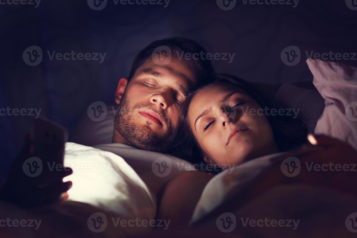 pareja joven usando teléfonos inteligentes en la cama por la noche foto