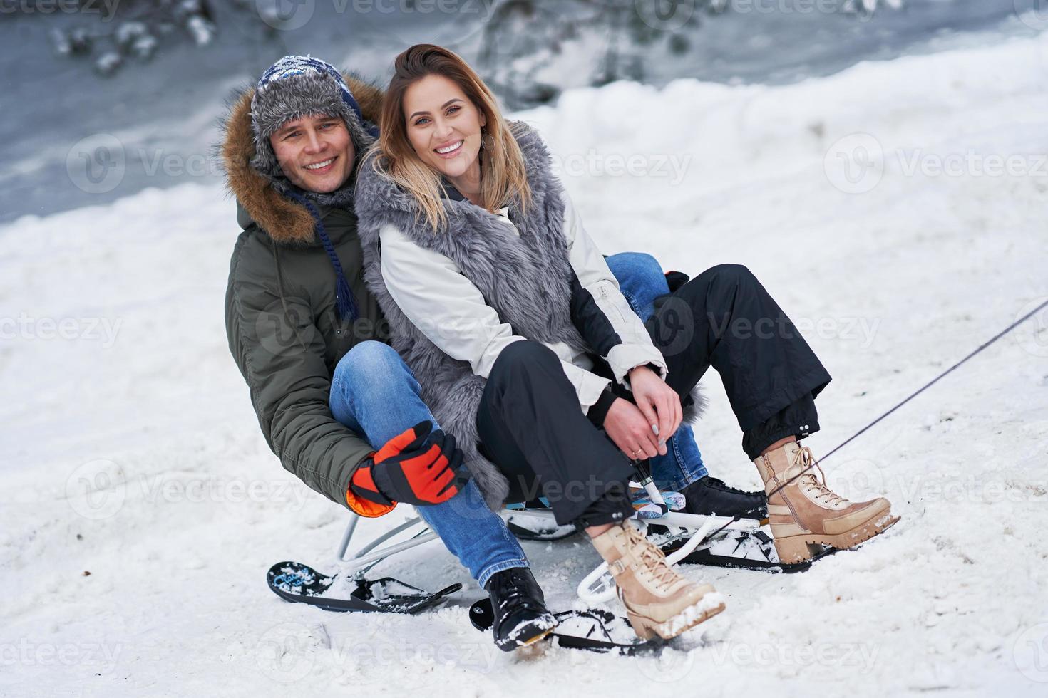 Couple having fun with sledge on snow in winter photo
