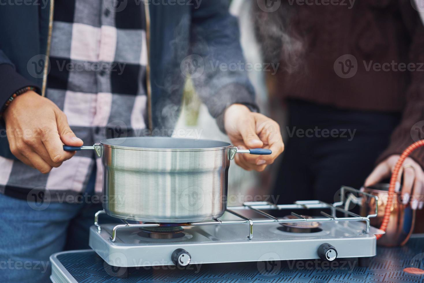 una pareja joven y agradable divirtiéndose acampando mientras cocinan y comen foto