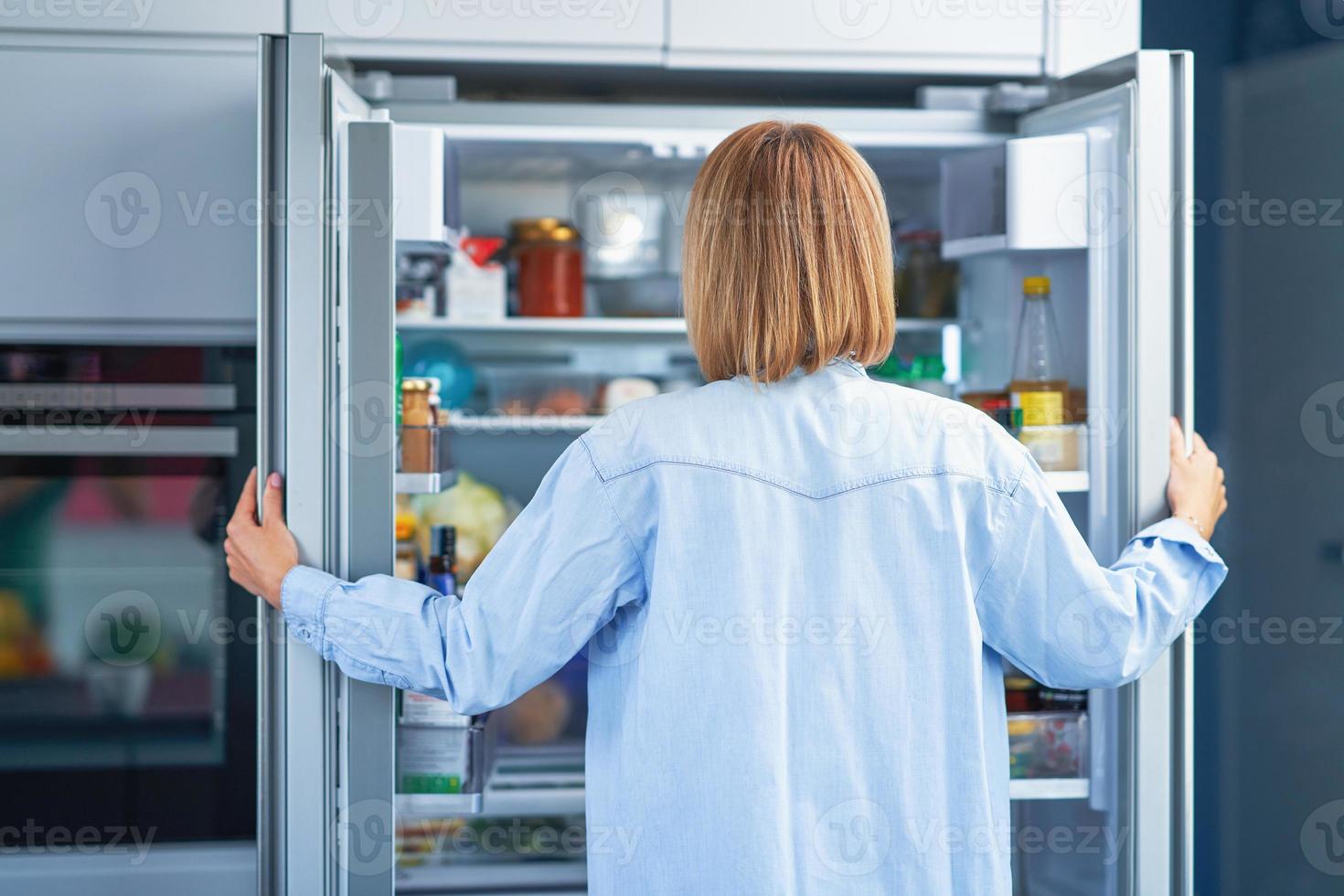 mujer adulta joven en la cocina con la nevera foto