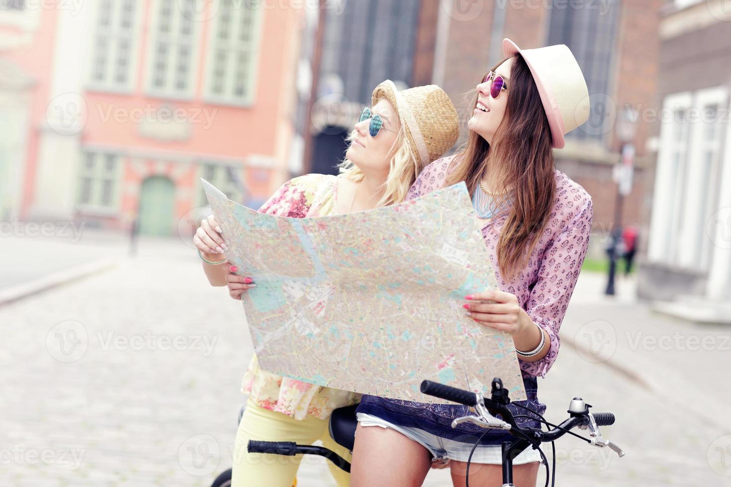 Two girl friends using map while riding tandem bicycle photo