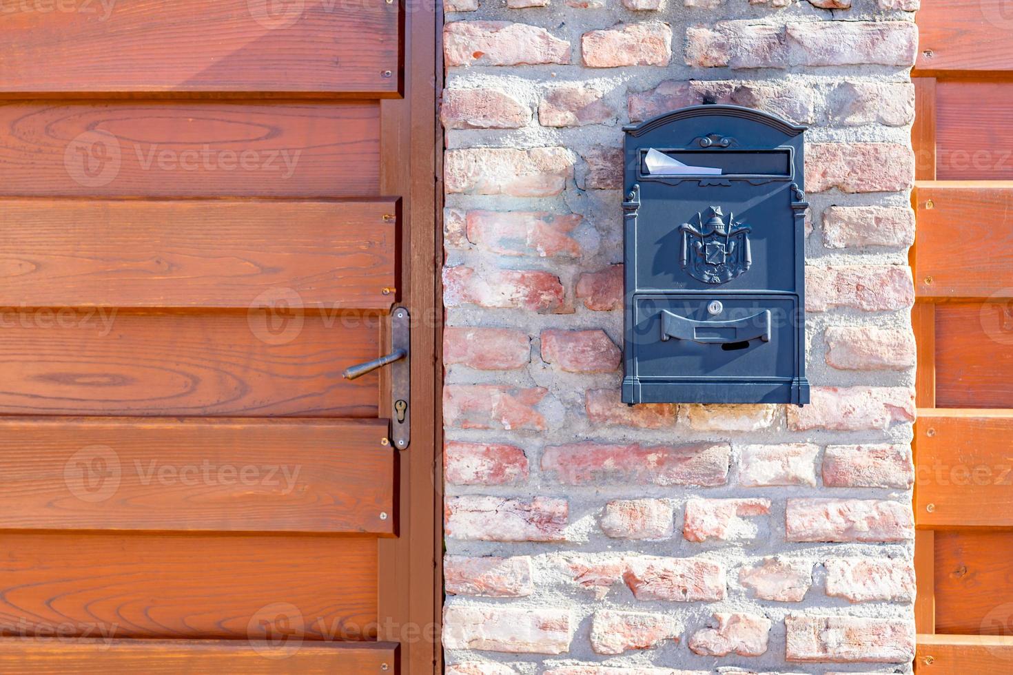 Old steel, iron mail box on stone brick wall, next to wooden fence on building or house door. Home related object, mail box photo