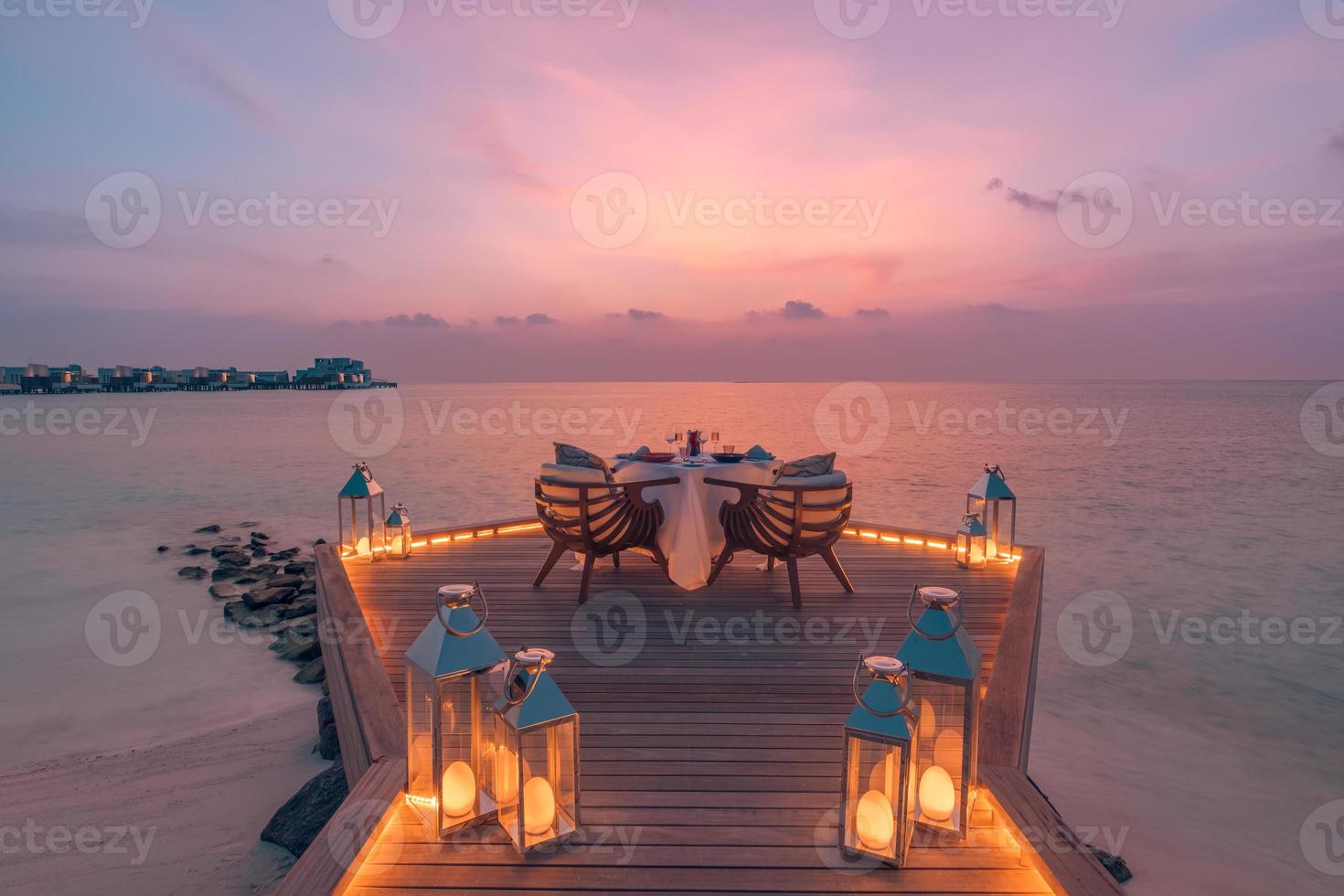 vista del paisaje marino bajo la luz del atardecer con mesa de comedor con piscina infinita alrededor. escapada tropical romántica para dos, concepto de pareja. sillas, comida y romance. comedor de destino de lujo, plantilla de luna de miel foto