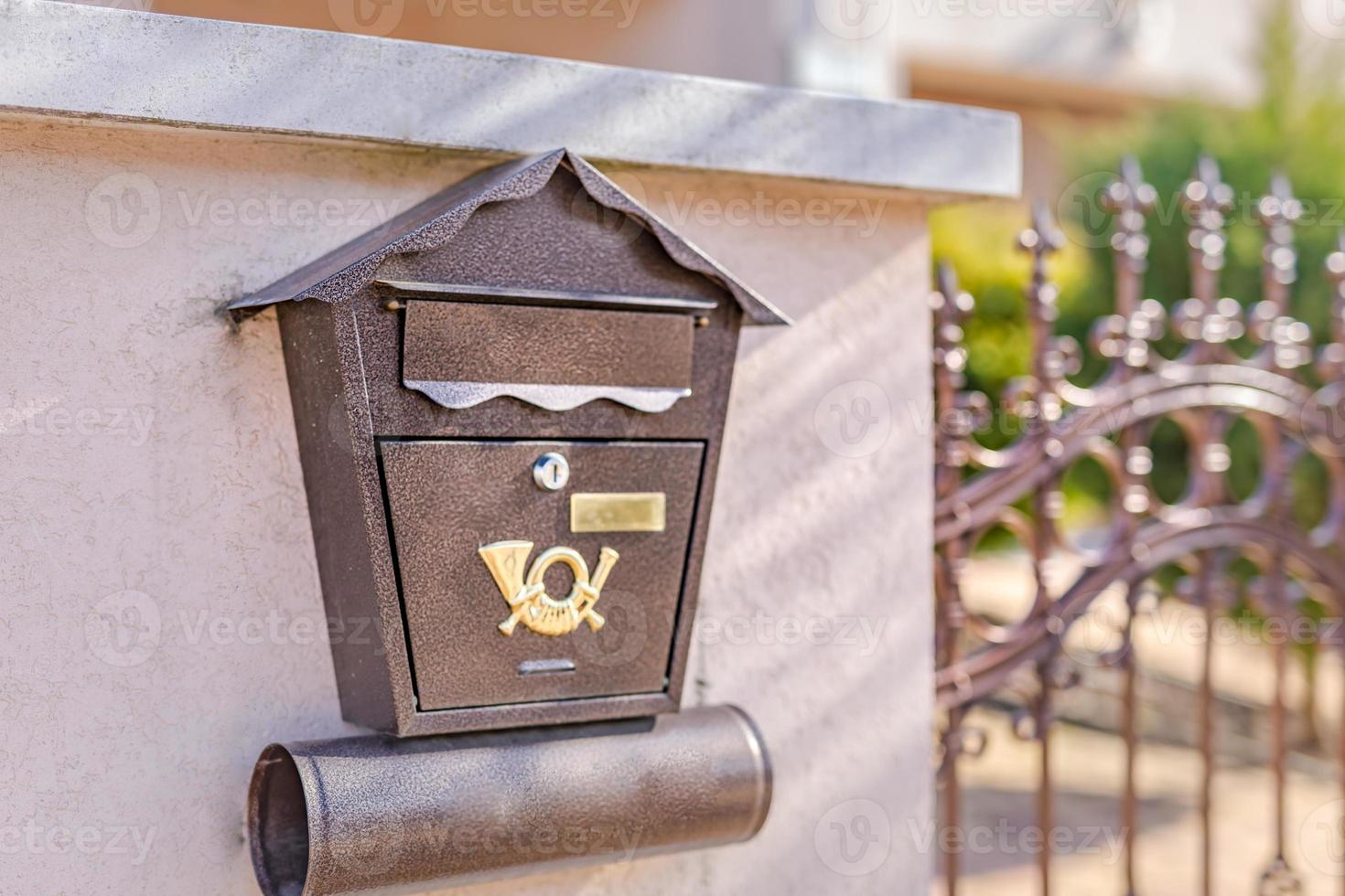 Brown postbox on modern house wall with iron fence. Mailbox, mail delivery photo