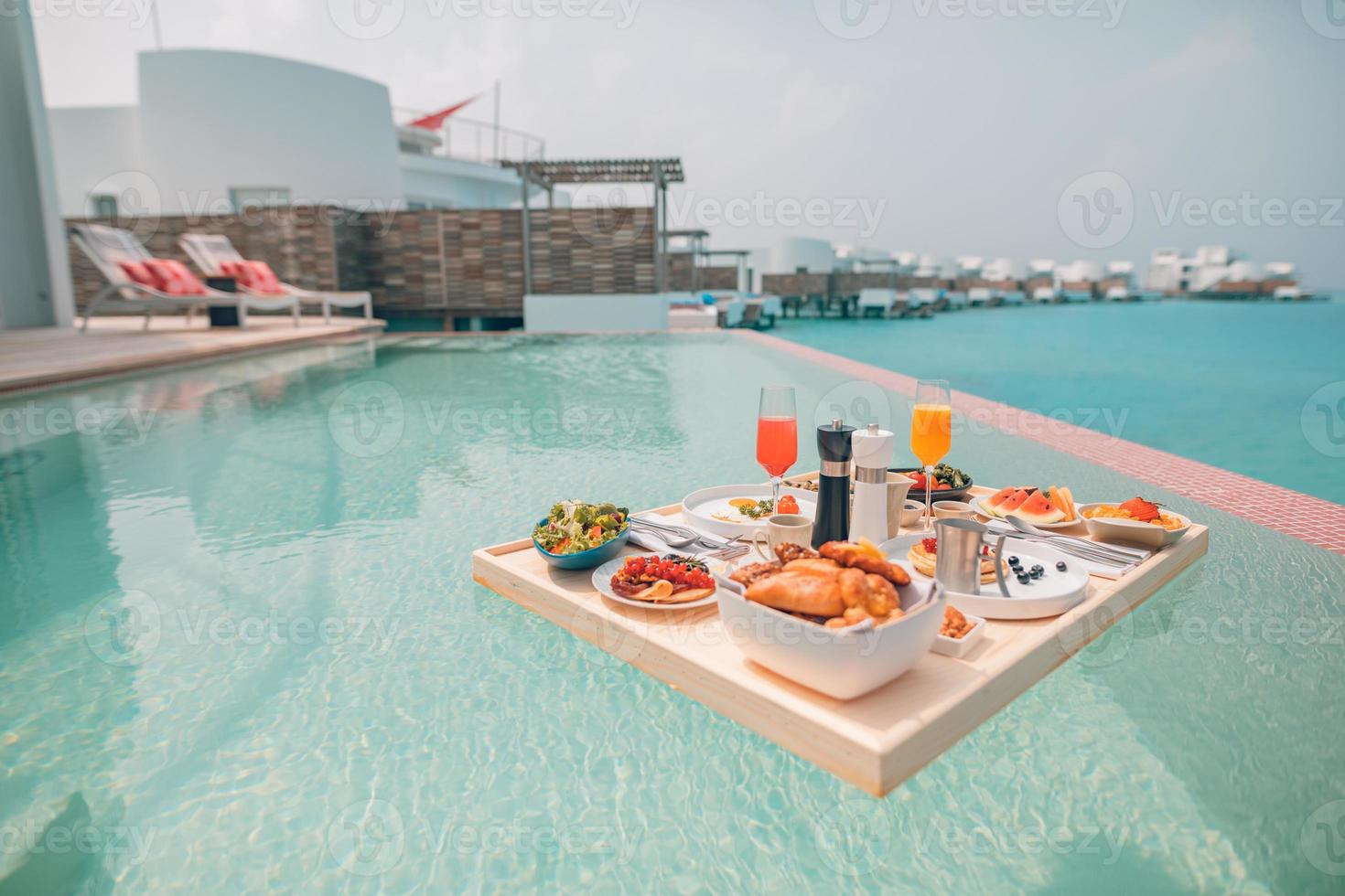 Breakfast in swimming pool, floating breakfast in luxurious tropical resort. Table relaxing on calm pool water, healthy breakfast and fruit plate by resort pool. Tropical couple beach luxury lifestyle photo