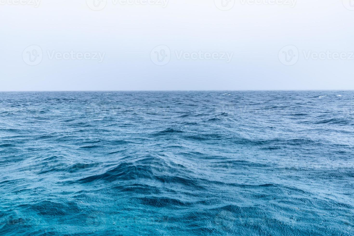 Rain over the stormy sea, blue ocean water and rain drops. Endless sea view horizon, fog and misty relaxing mood. Abstract seaside photo