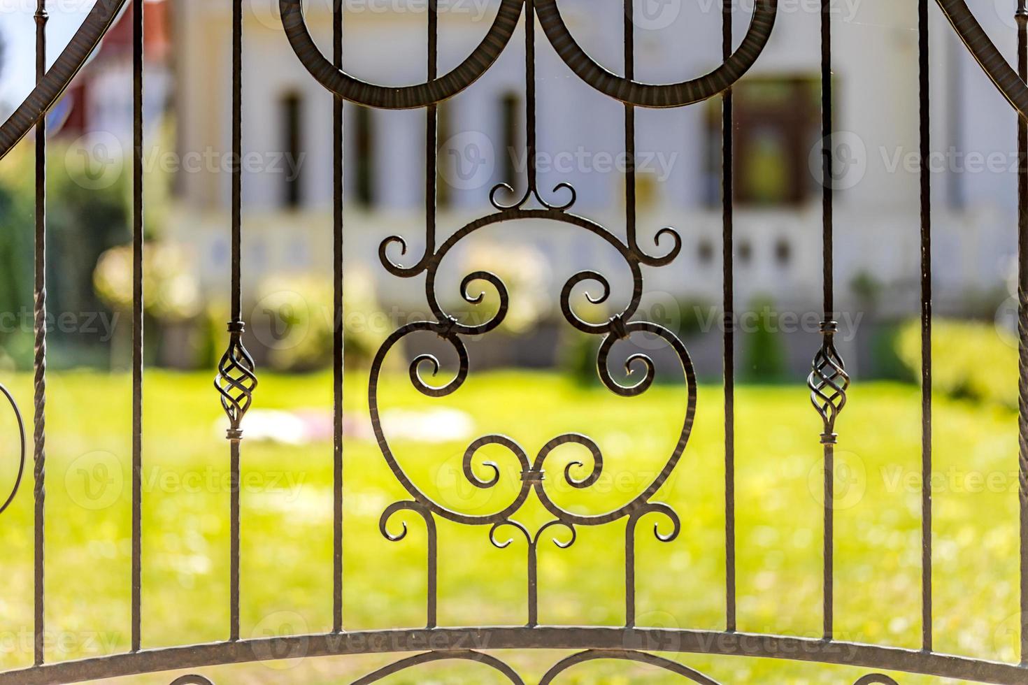 Railings close-up, wrought iron backyard fence with decorative middle and green grass in background with luxury house, villa on warm sunny spring day photo