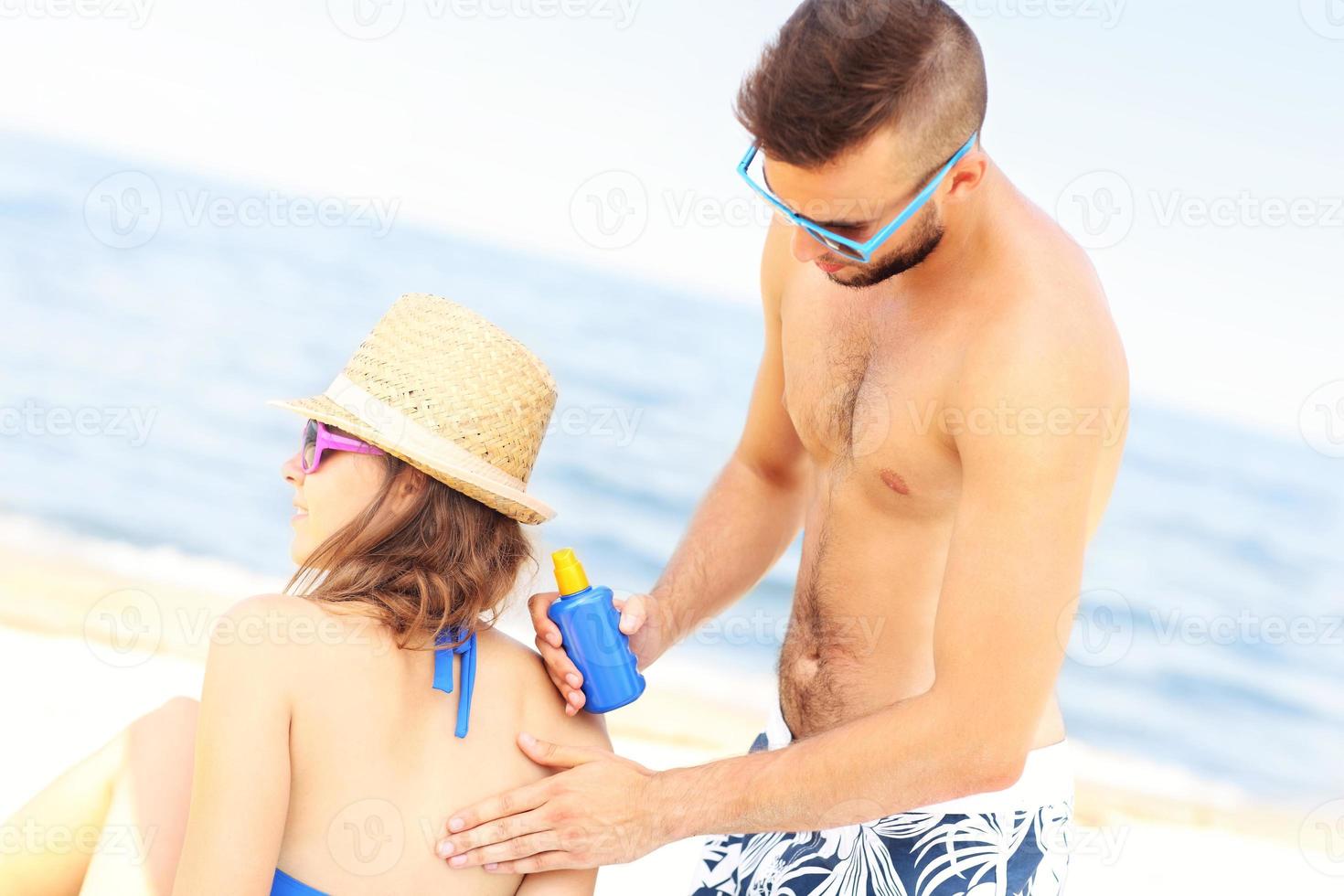 Man applying sunscreen on the back of his woman photo