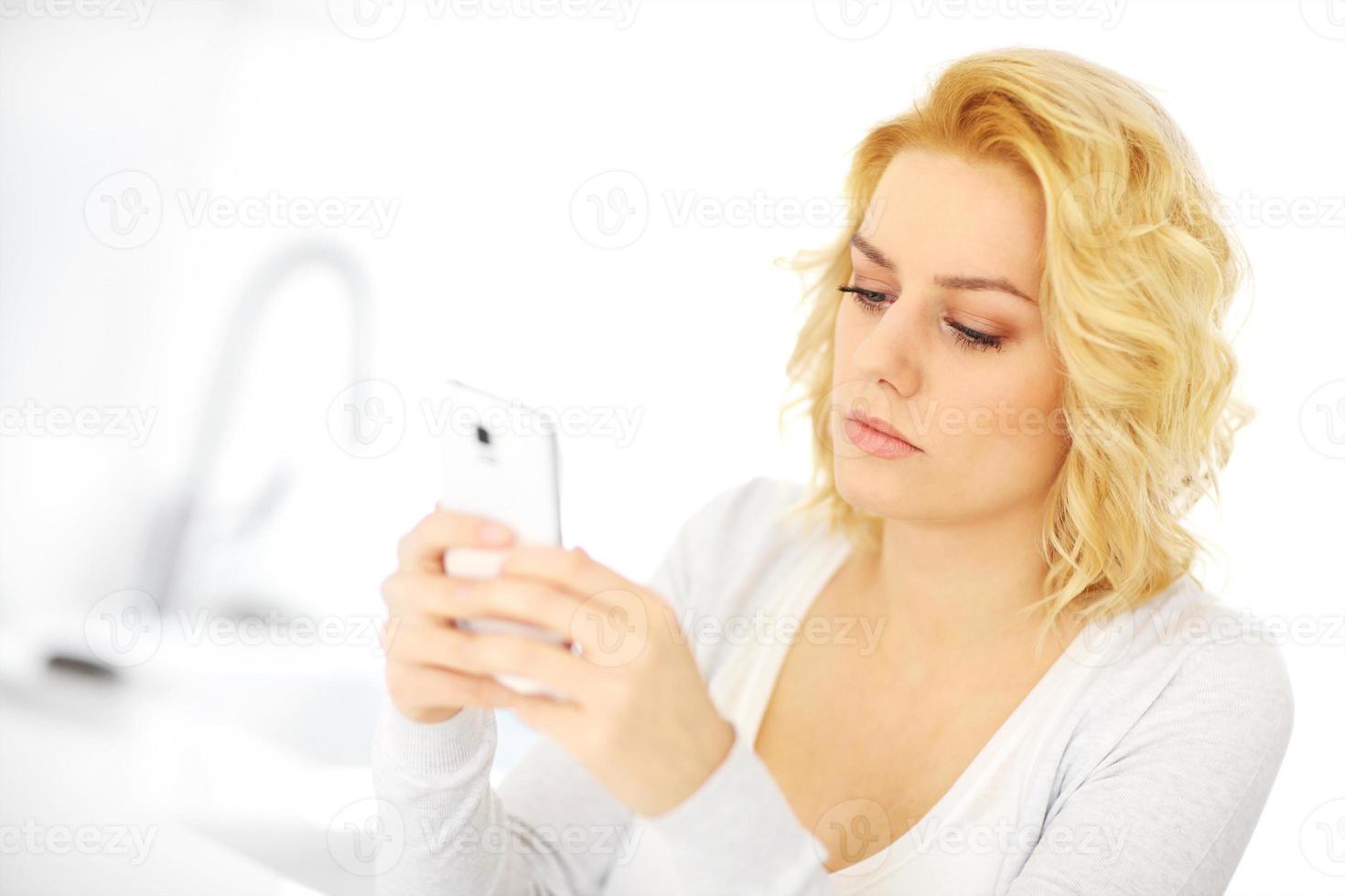 Young woman with smartphone in the kitchen photo