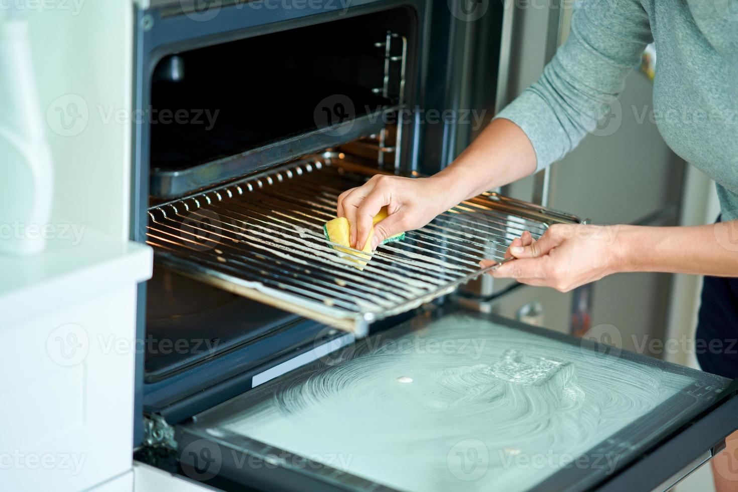 mujer joven limpiando el horno en la cocina foto