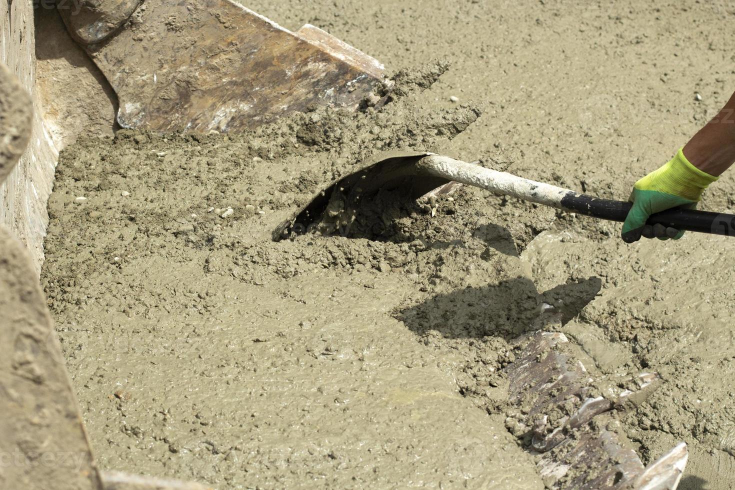 Shovel and cement. Shovel in hands of worker. Cement mixture spilled on road. Cleaning of building material. photo