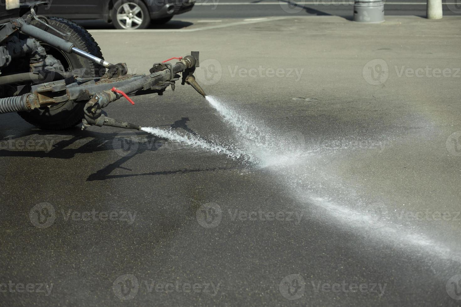 carretera de lavado de autos. tractor vierte agua. lavar la suciedad del asfalto. chorro de agua de la máquina. foto