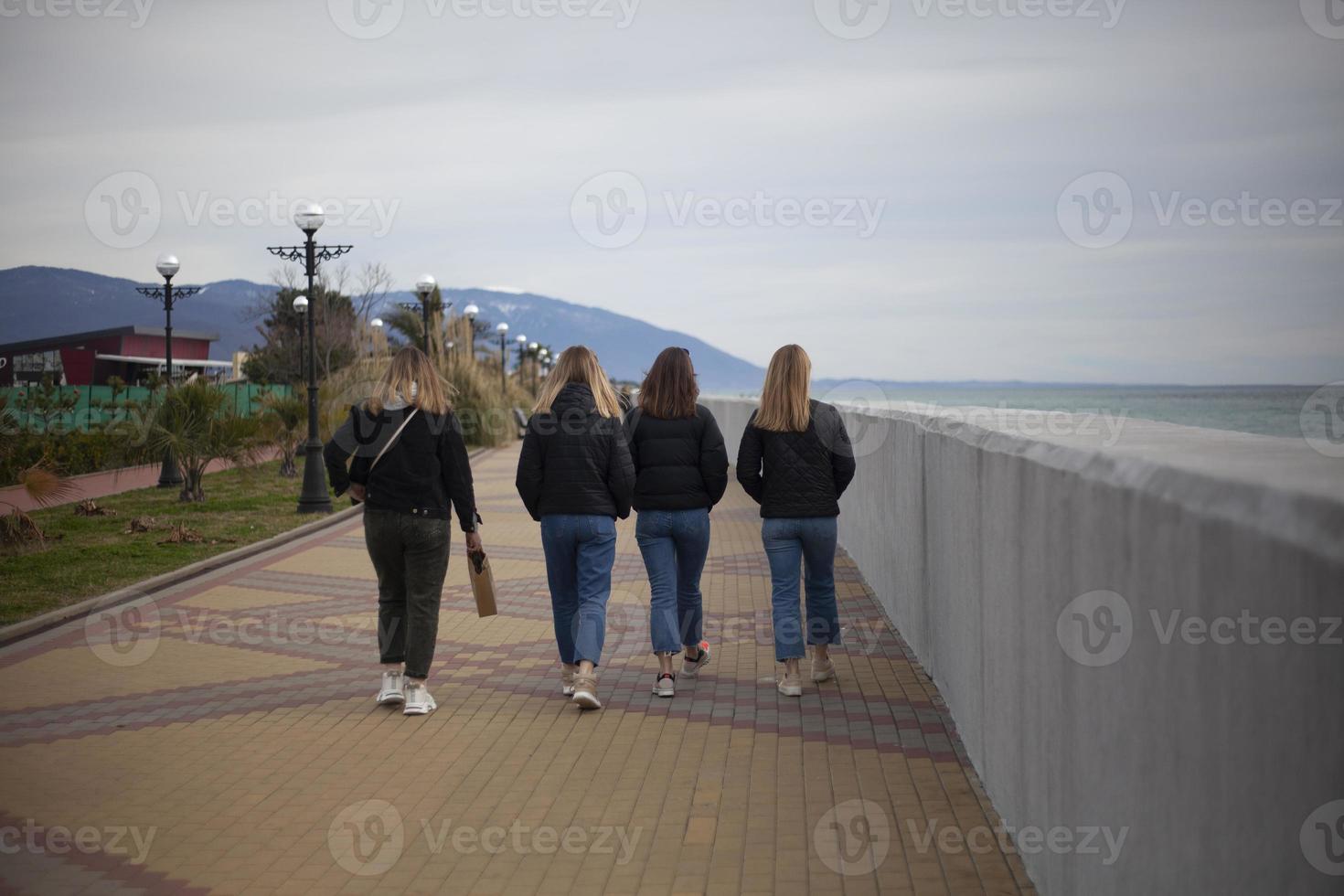 Young girls walk along the arranged promenade by the sea. Friends walk along the stone promenade. Shooting teenagers from the back. photo