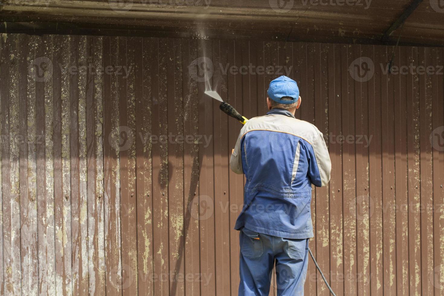 Worker washes fence. Flow of water. Washing off dirt from fence. Person holds hose. photo