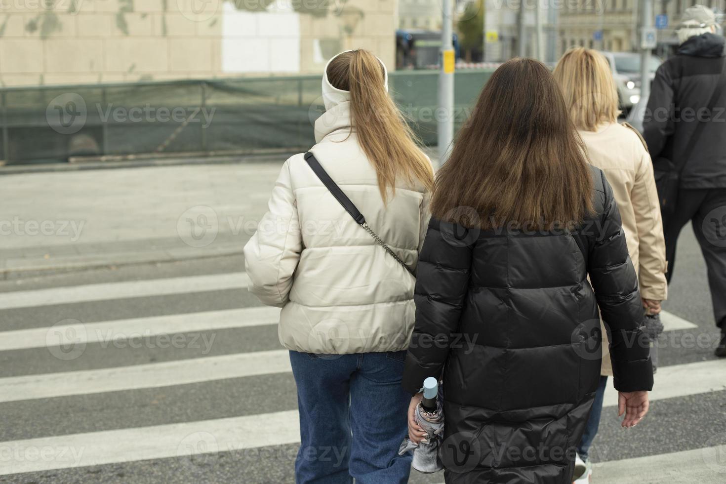 Girls walking on pedestrian crossing. Crossing road. People on street in warm clothes. photo